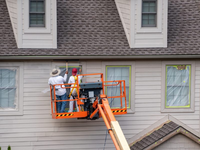 Two home painters in articulating boom lift spray painting townhouse