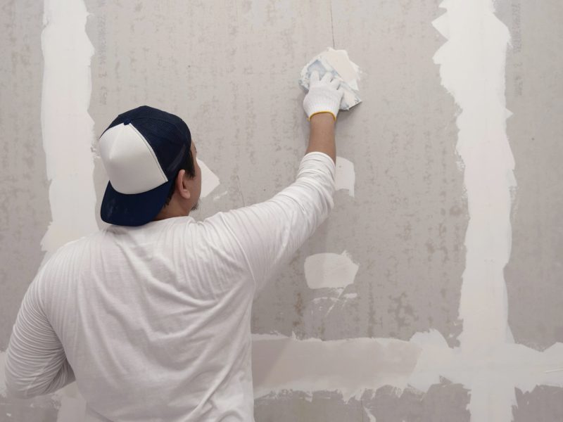 Plasterwork and wall painting preparation. Asian male applying plaster or filling drywall patch